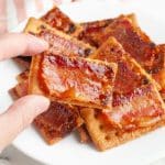 Hand holding a cracker topped with bacon.