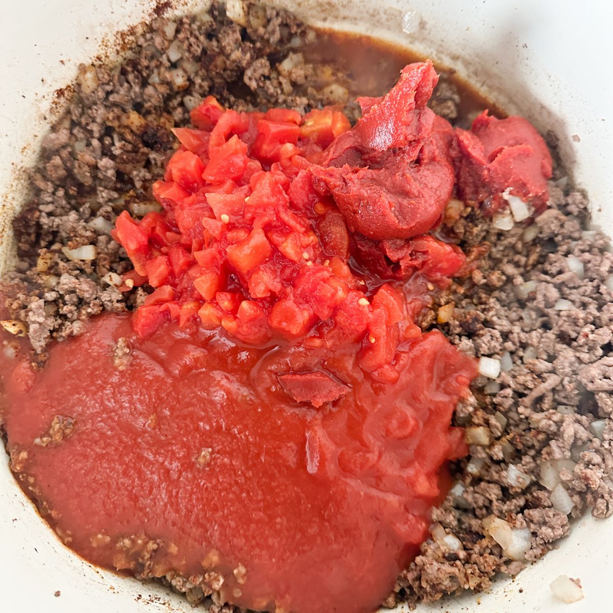 Ground beef with tomato sauce and diced tomatoes in a pot. 