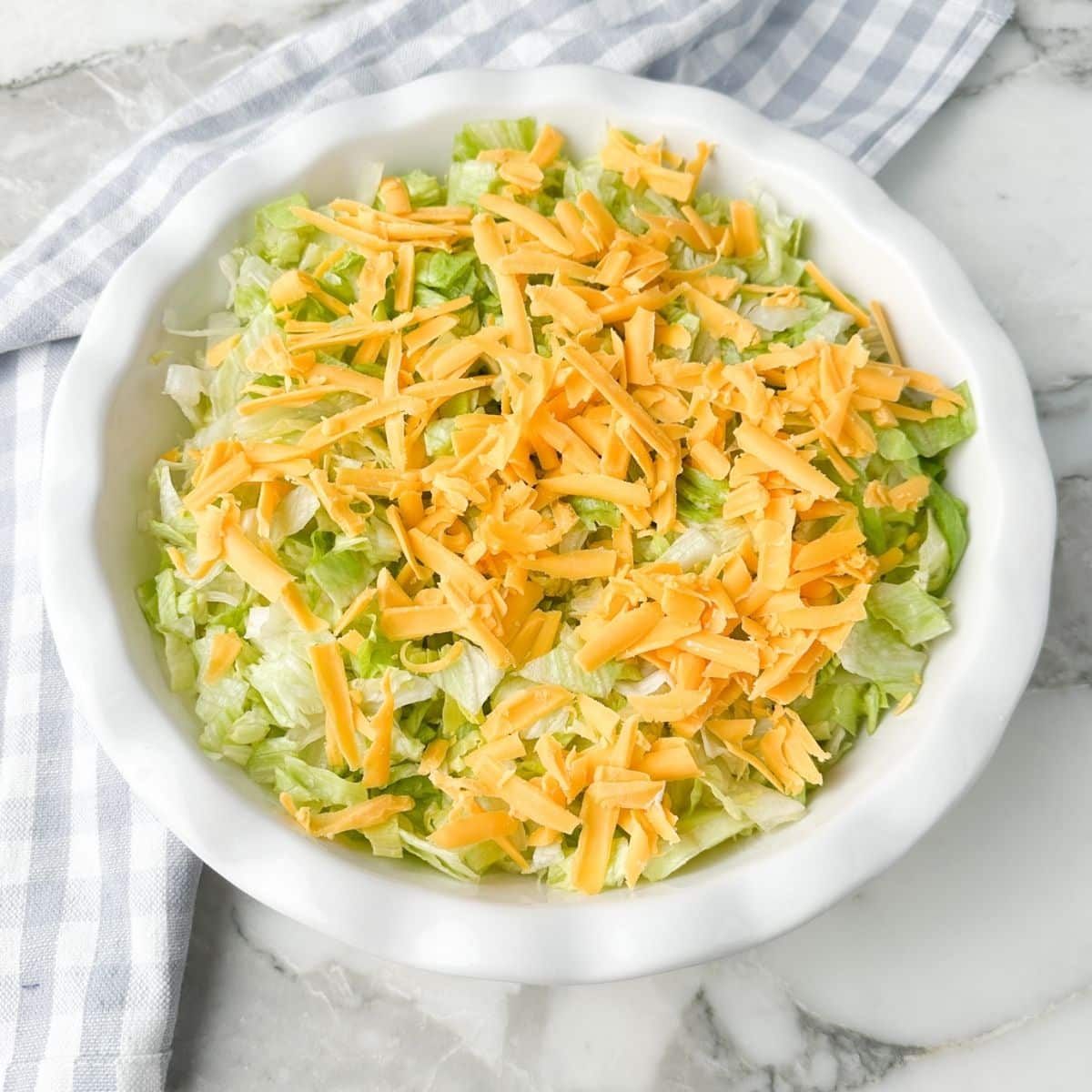 Pie plate with cream cheese, lettuce, and shredded cheese. 