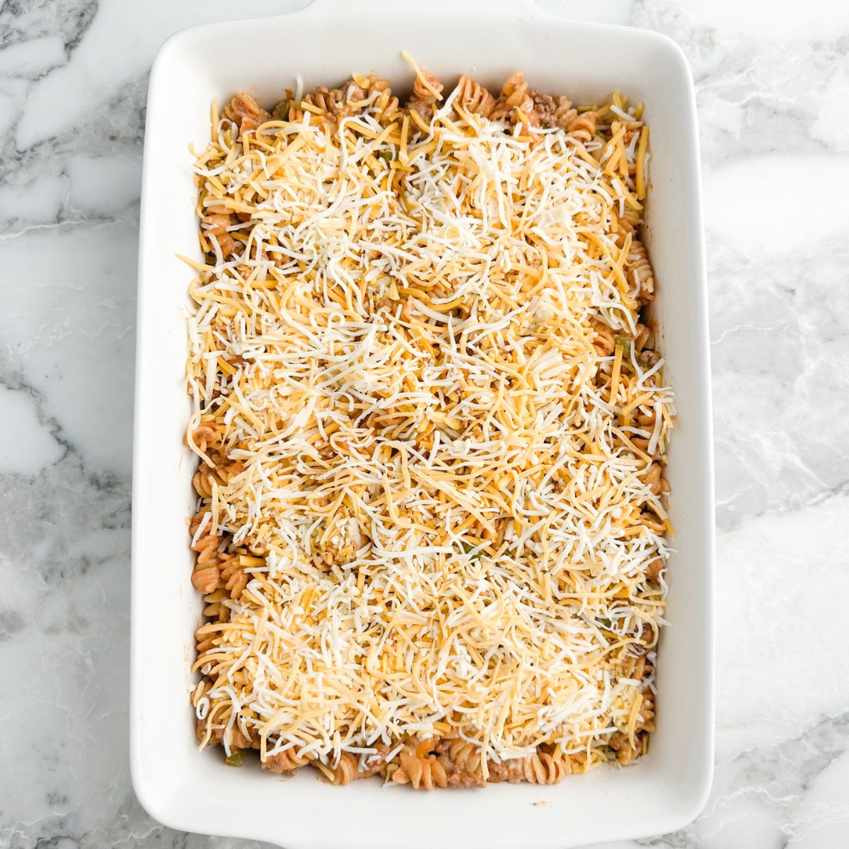 Casserole dish with pasta mixture topped with shredded cheese.