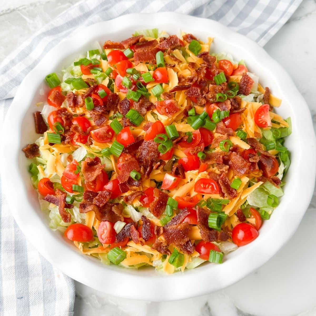 Pie plate with lettuce, shredded cheese, bacon crumbles, and tomatoes. 