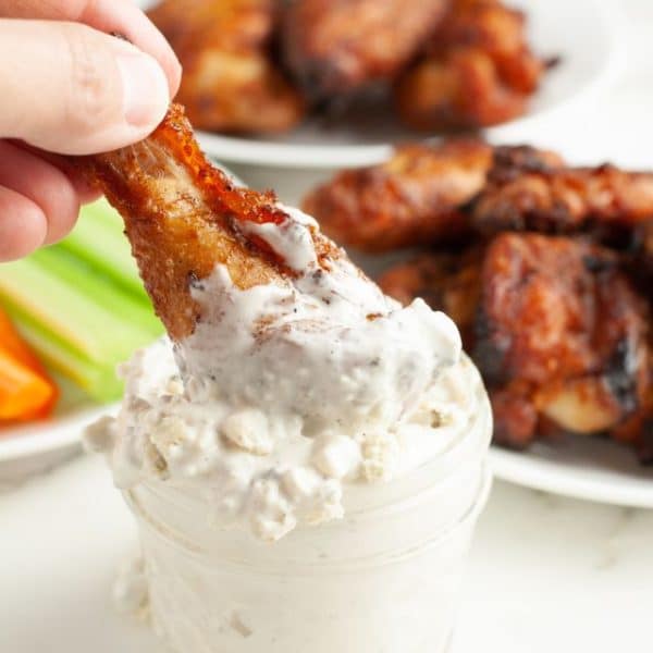 Chicken wing dipping into blue cheese sauce.