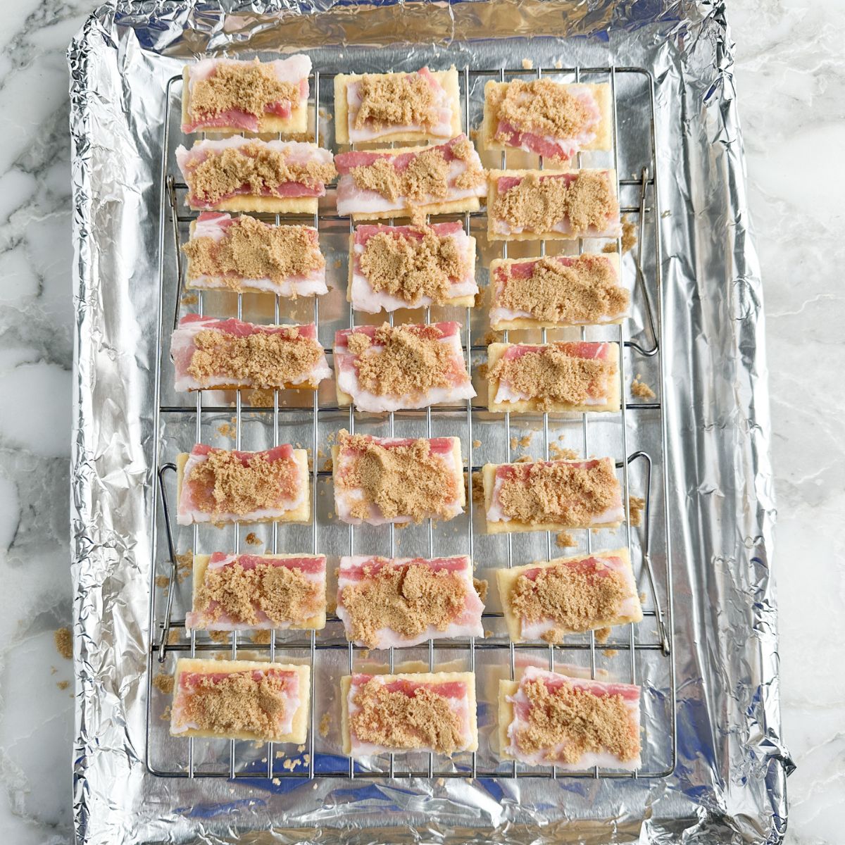 Baking sheet with crackers topped with bacon and brown sugar.