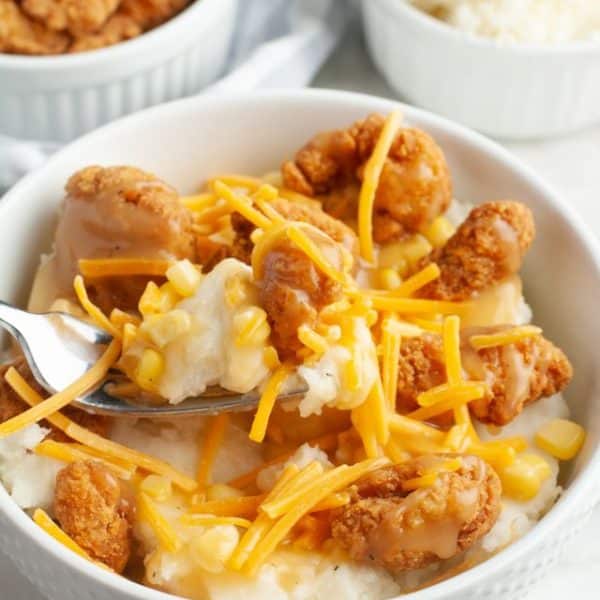 Bowl with mashed potatoes topped with fried chicken and shredded cheese.