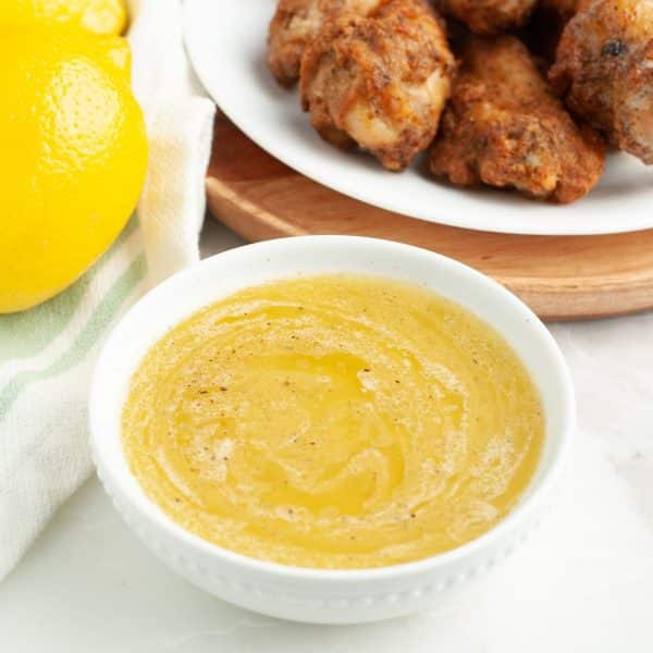 Bowl of lemon pepper sauce with a plate of chicken wings.