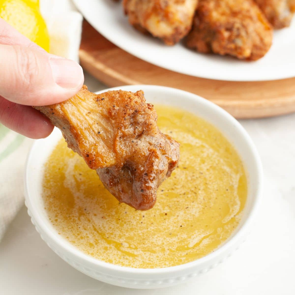 Bowl of lemon pepper sauce with a chicken wing dipping in. 