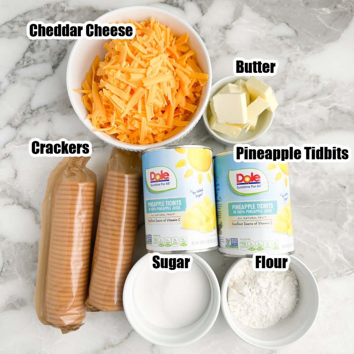 Bowl of shredded cheese, butter, sugar, flour, cans of pineapple, and crackers. 