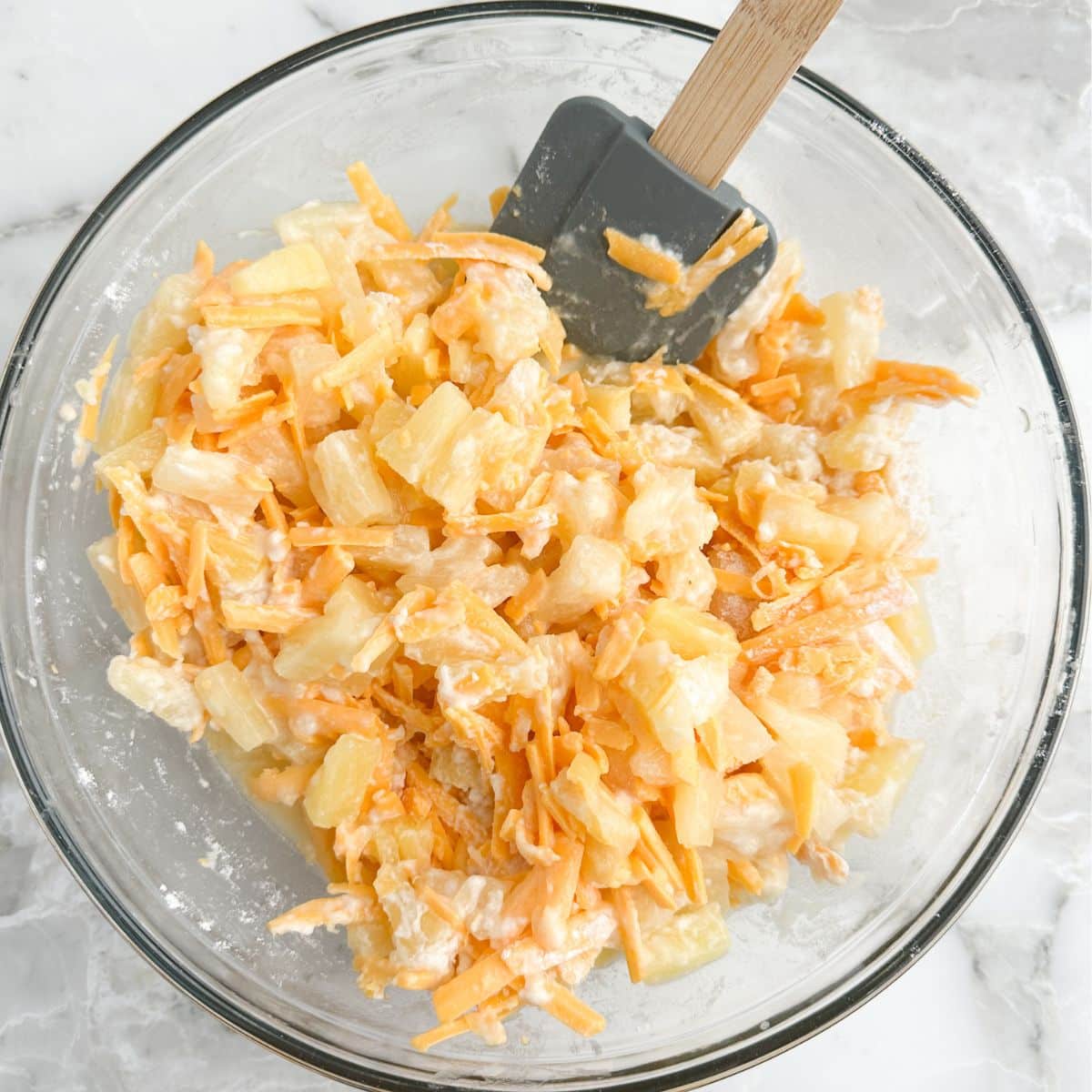 Bowl of cheese, pineapple tidbits, and a spatula. 