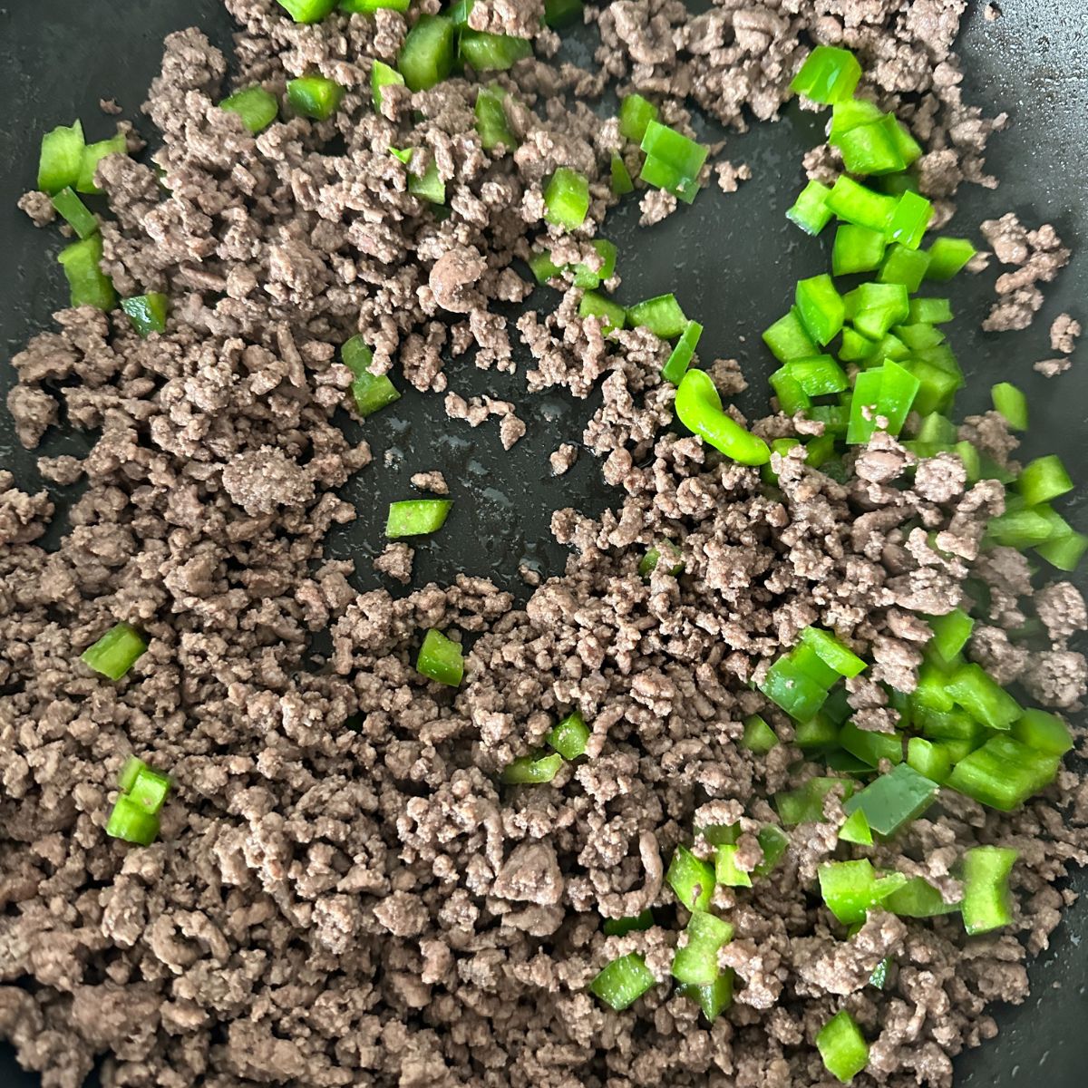 Ground beef and diced green pepper in a skillet. 