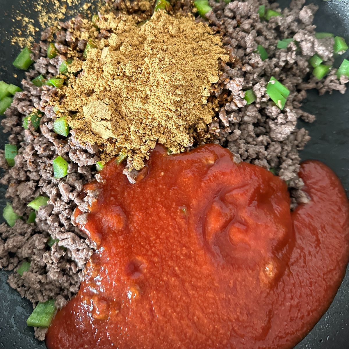 Ground beef, taco seasonings, and tomato sauce in a skillet. 