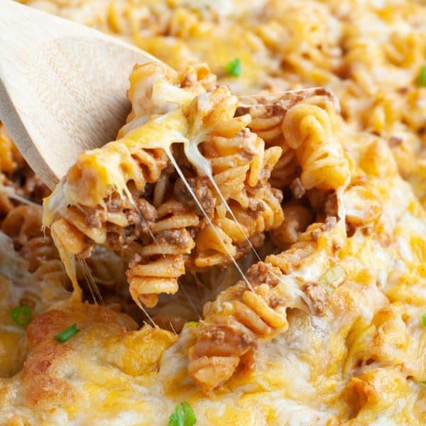 Wooden spoon with rotini pasta cheese casserole.