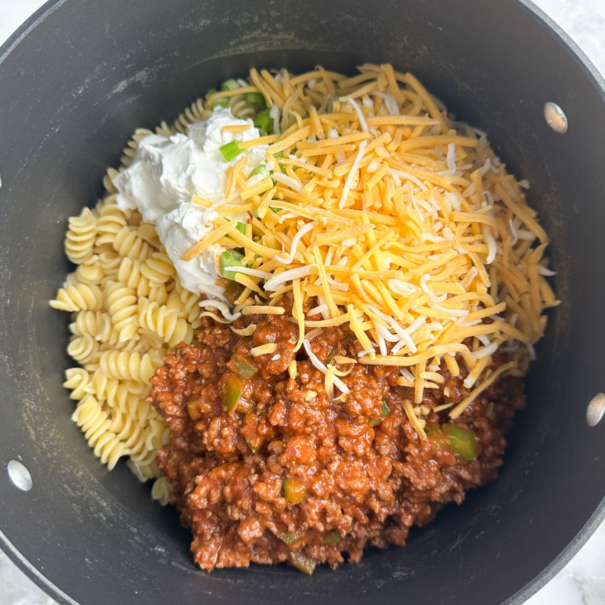Pot with ground beef, pasta, shredded cheese, and sour cream. 