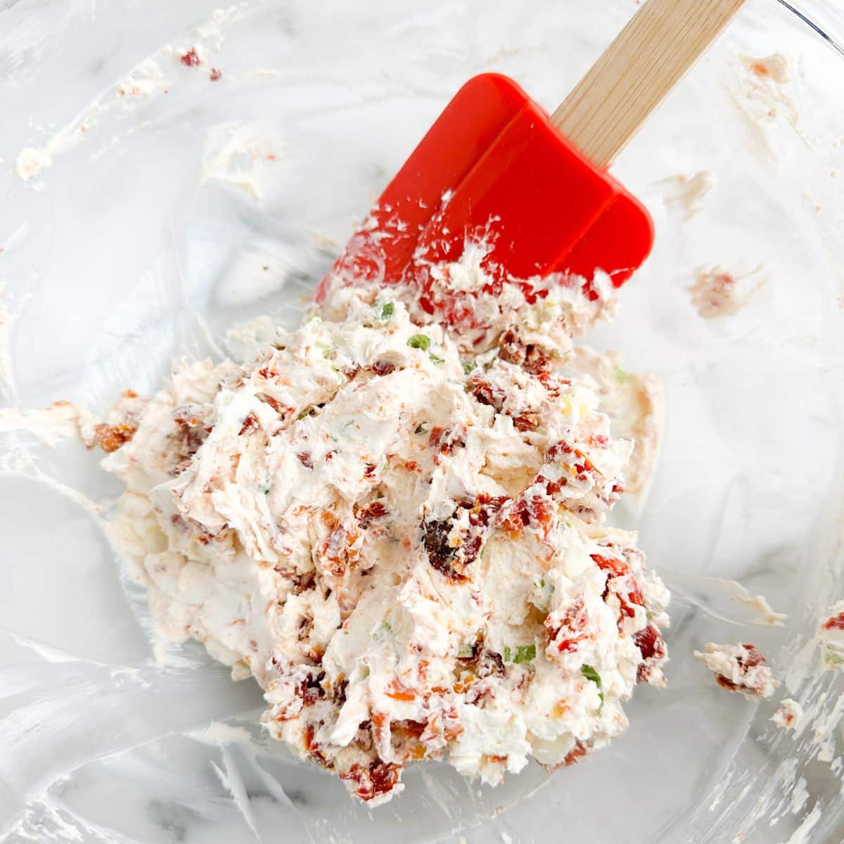 Bowl with cream cheese mixed with sun dried tomatoes and a spatula.
