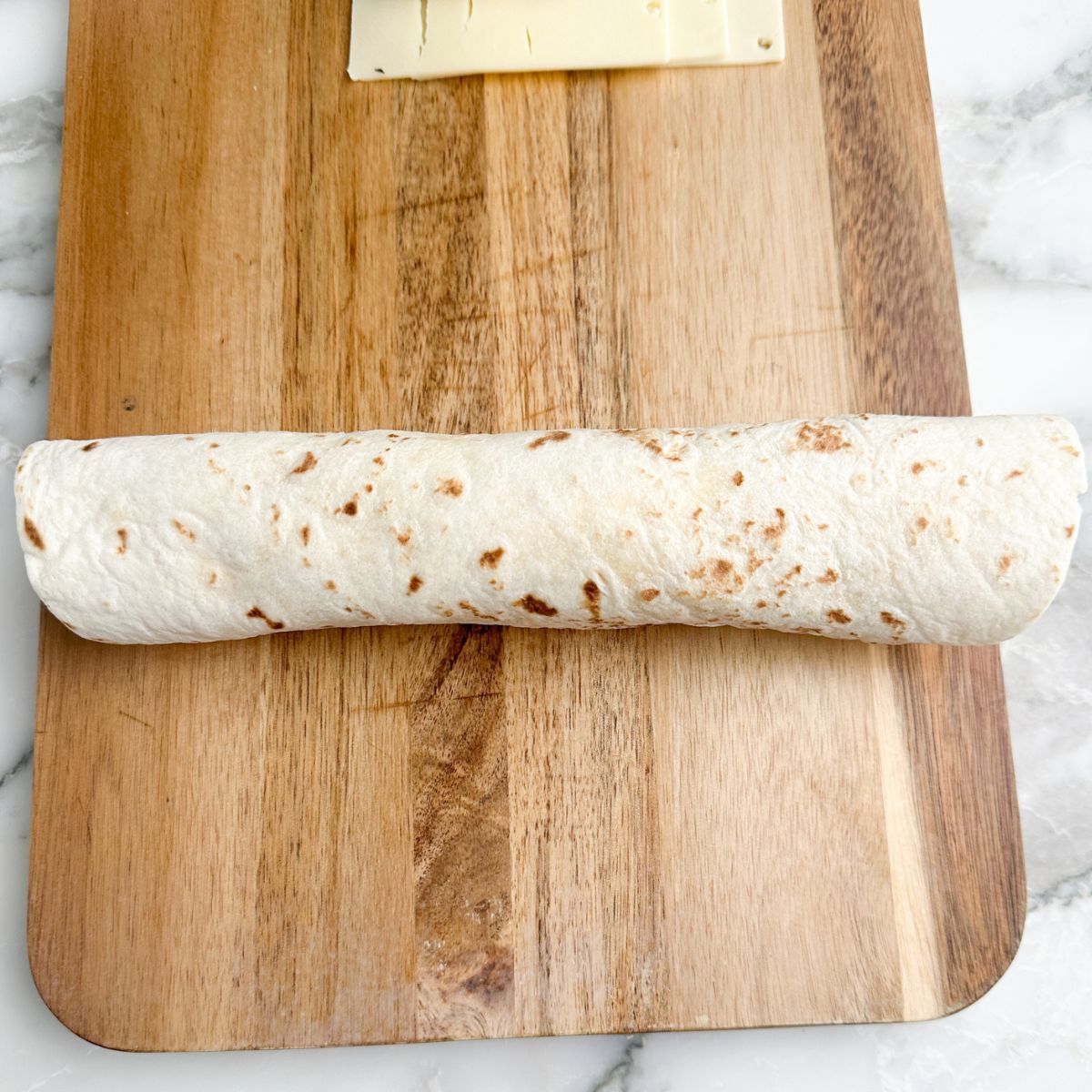 Rolled up tortilla pinwheel on a cutting board. 
