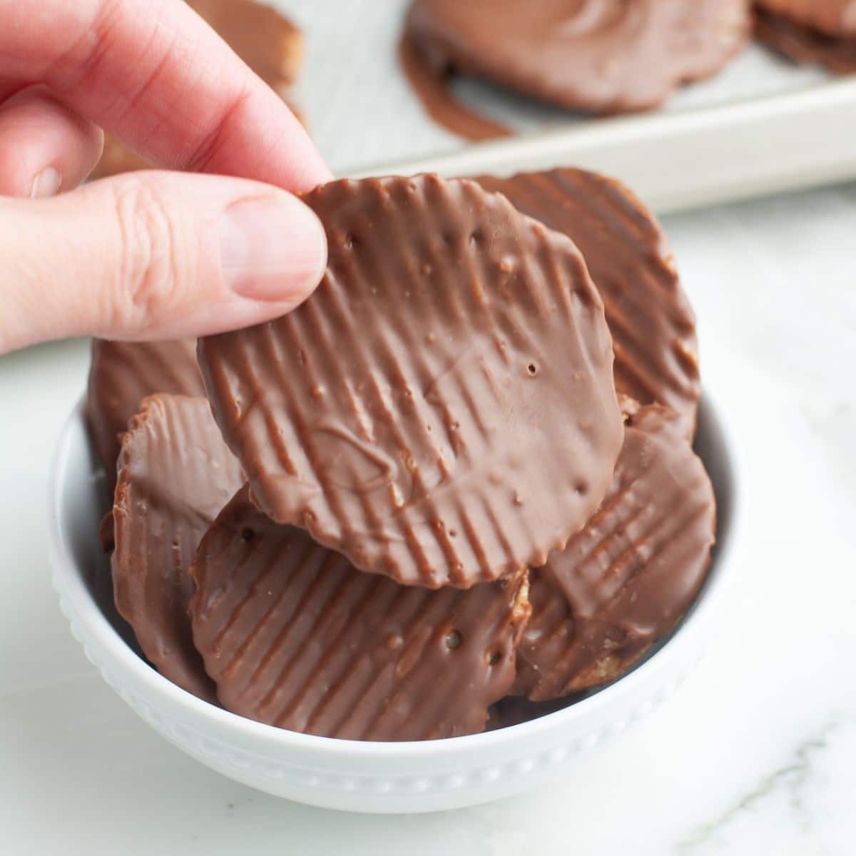 Hand holding a chocolate covered potato chip.