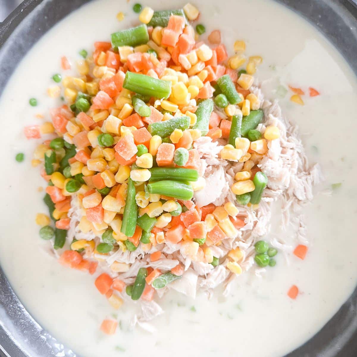Skillet with a cream sauce, shredded chicken, and mixed vegetables.