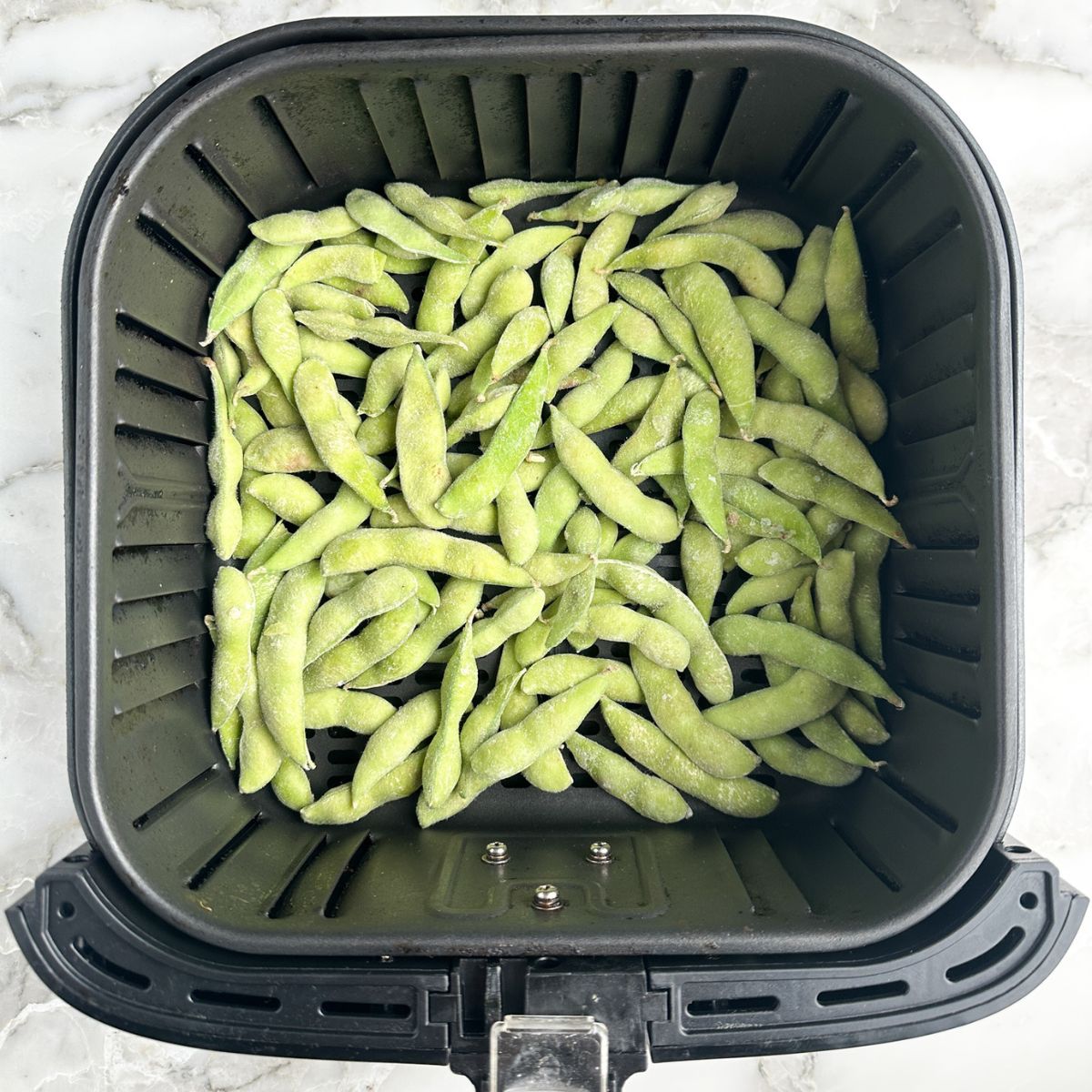 Edamame in an air fryer basket.