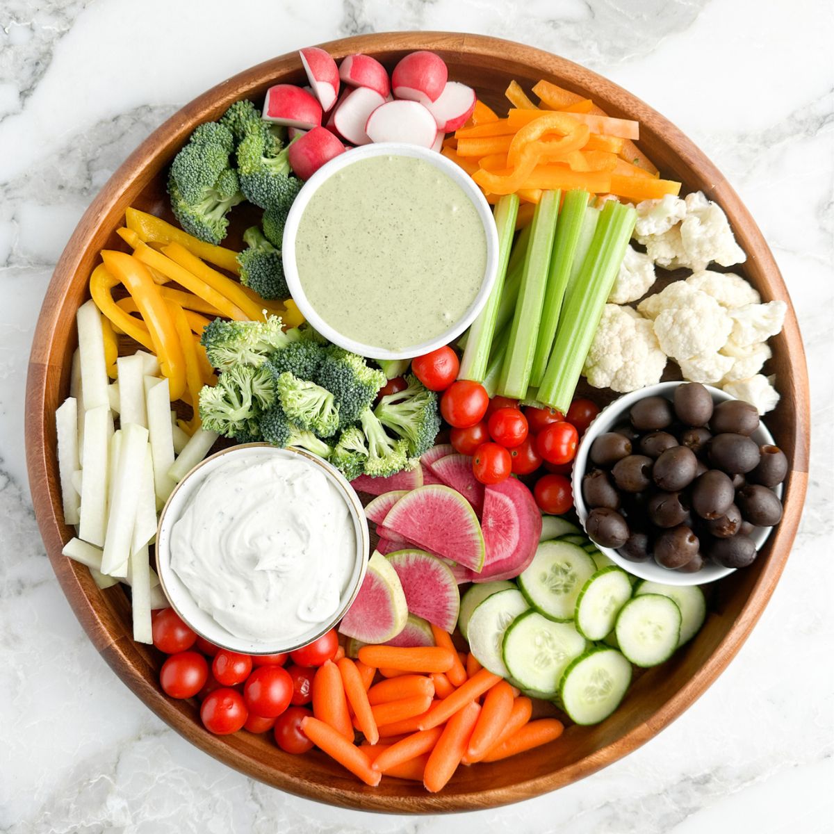 Round platter with cut up vegetables and 2 bowls of ranch dip.