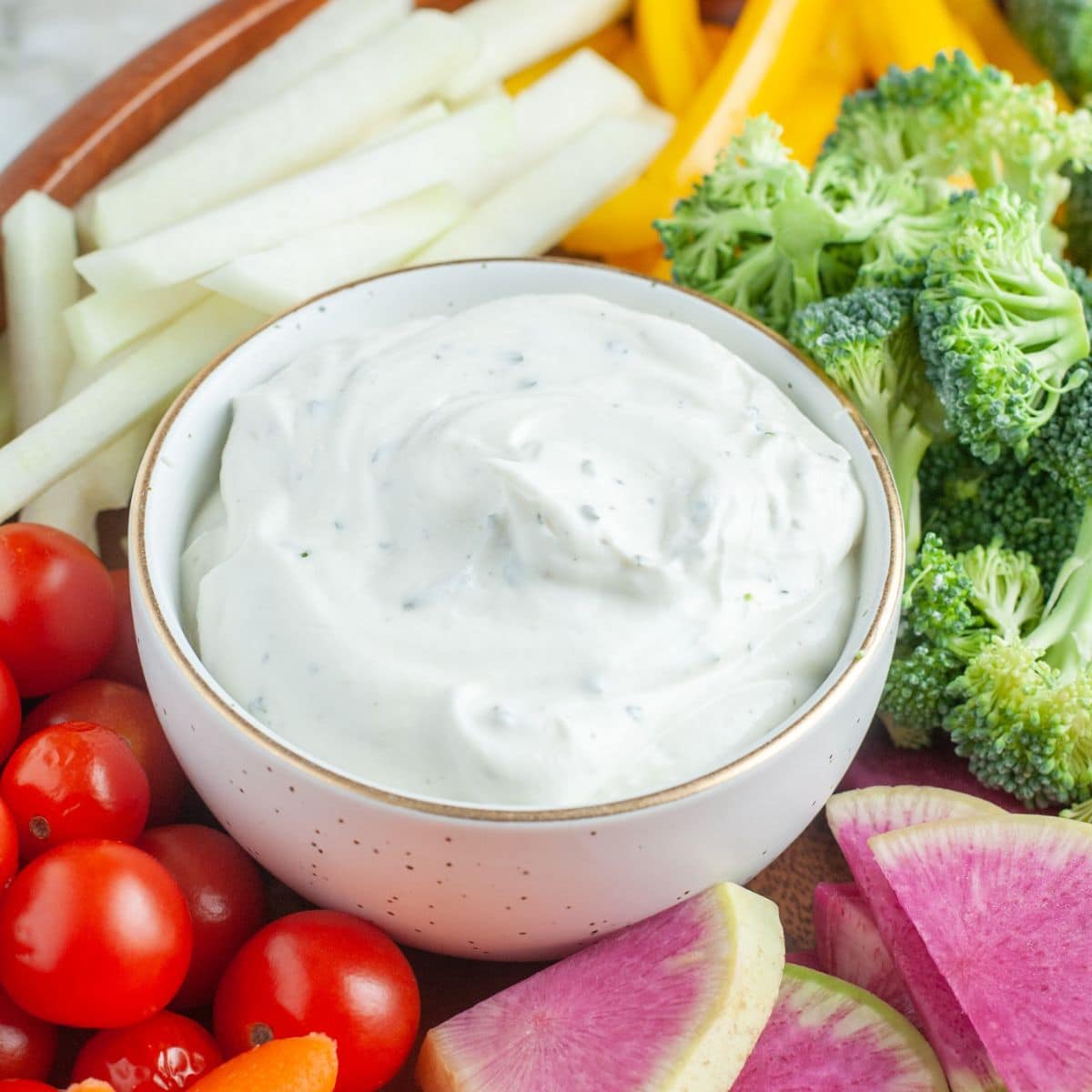 Bowl of ranch dip surrounded by vegetables. 