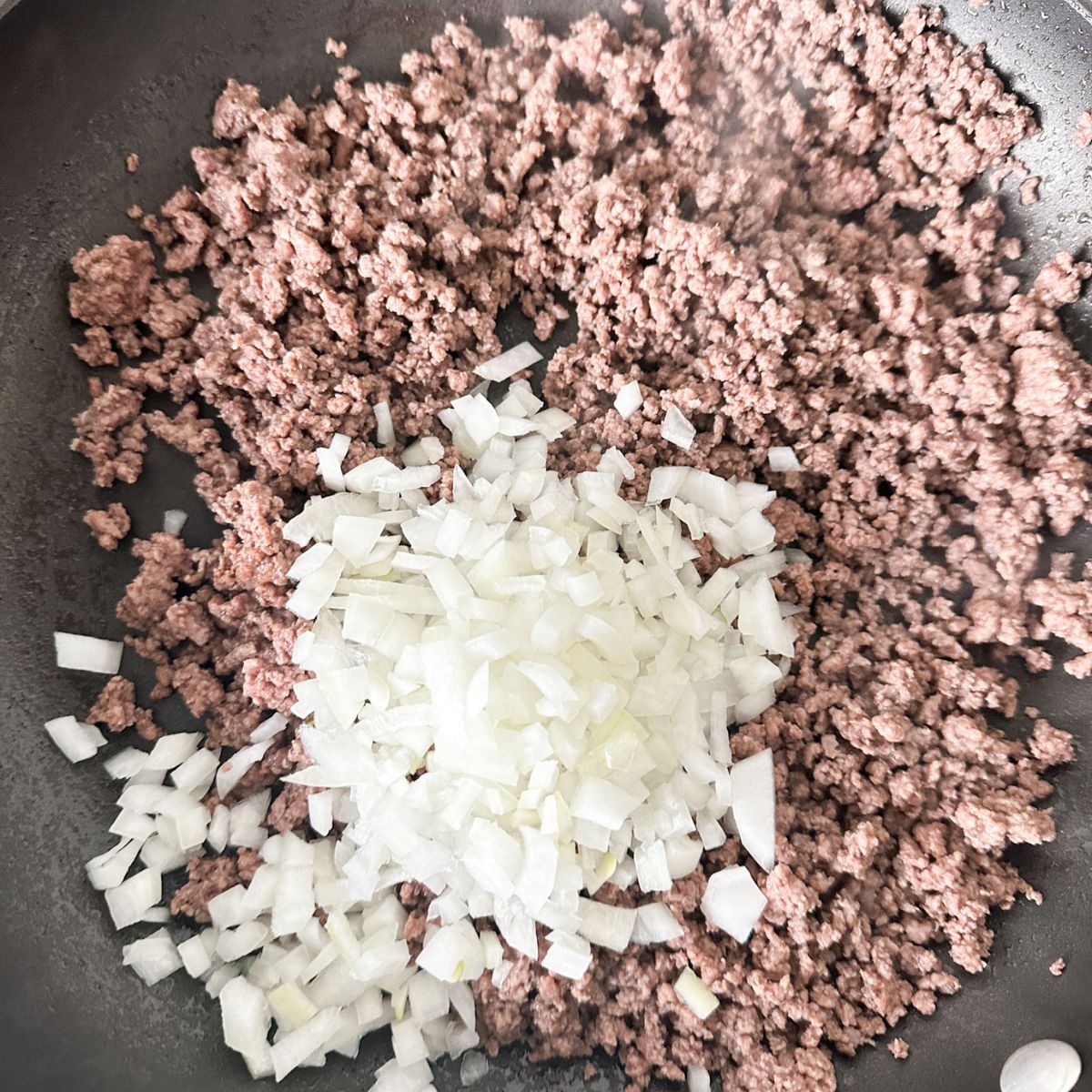 Skillet with ground beef and diced onion.