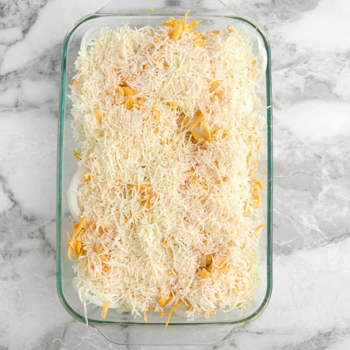 Baking dish with sliced onions and shredded cheese. 