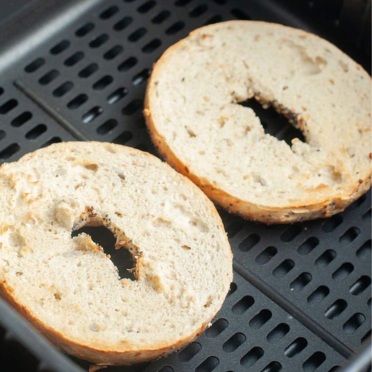 Bagel halves in air fryer basket.