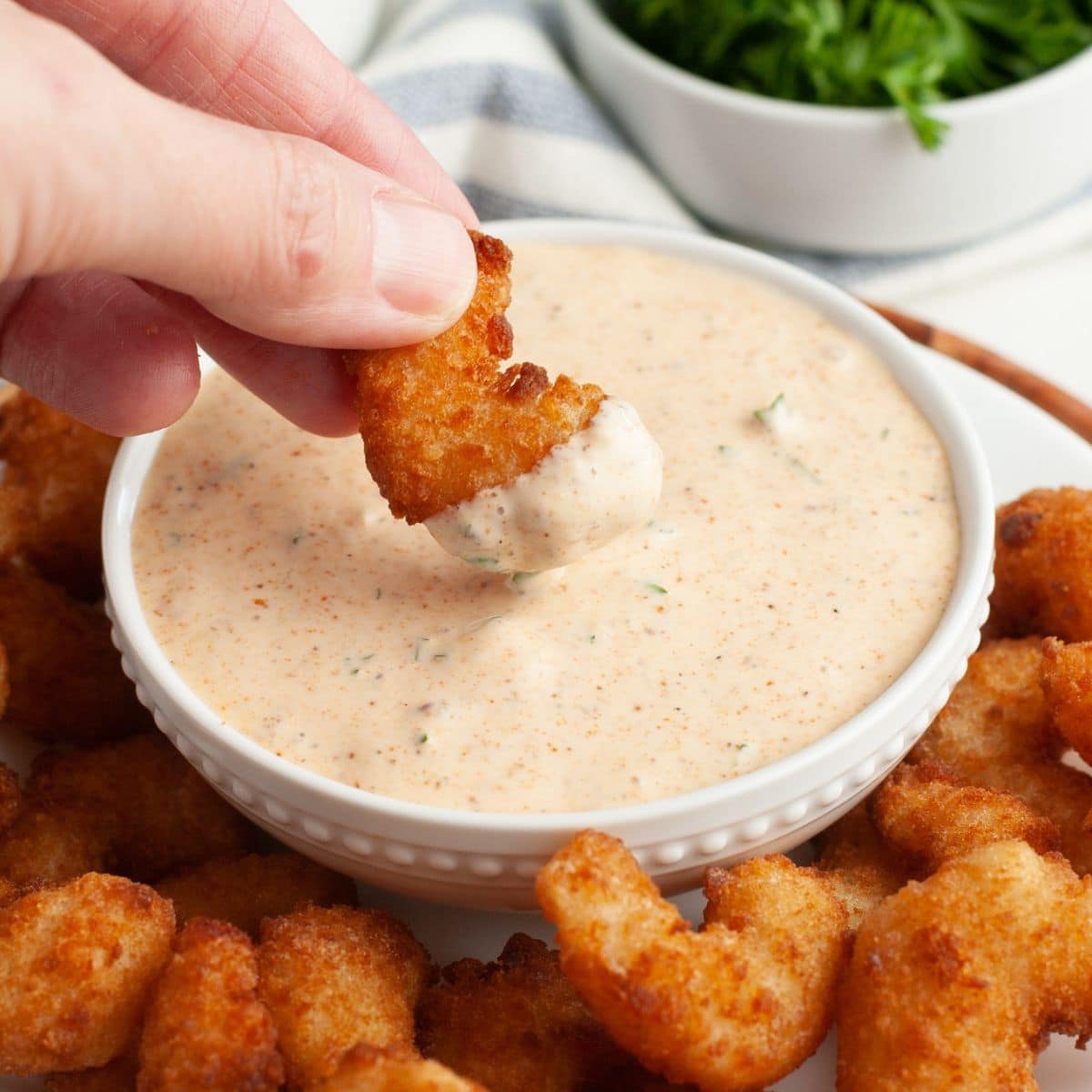 Bowl with remoulade sauce and a fried shrimp dipping into the sauce. 