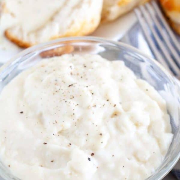 Bowl of white gravy and a biscuit.