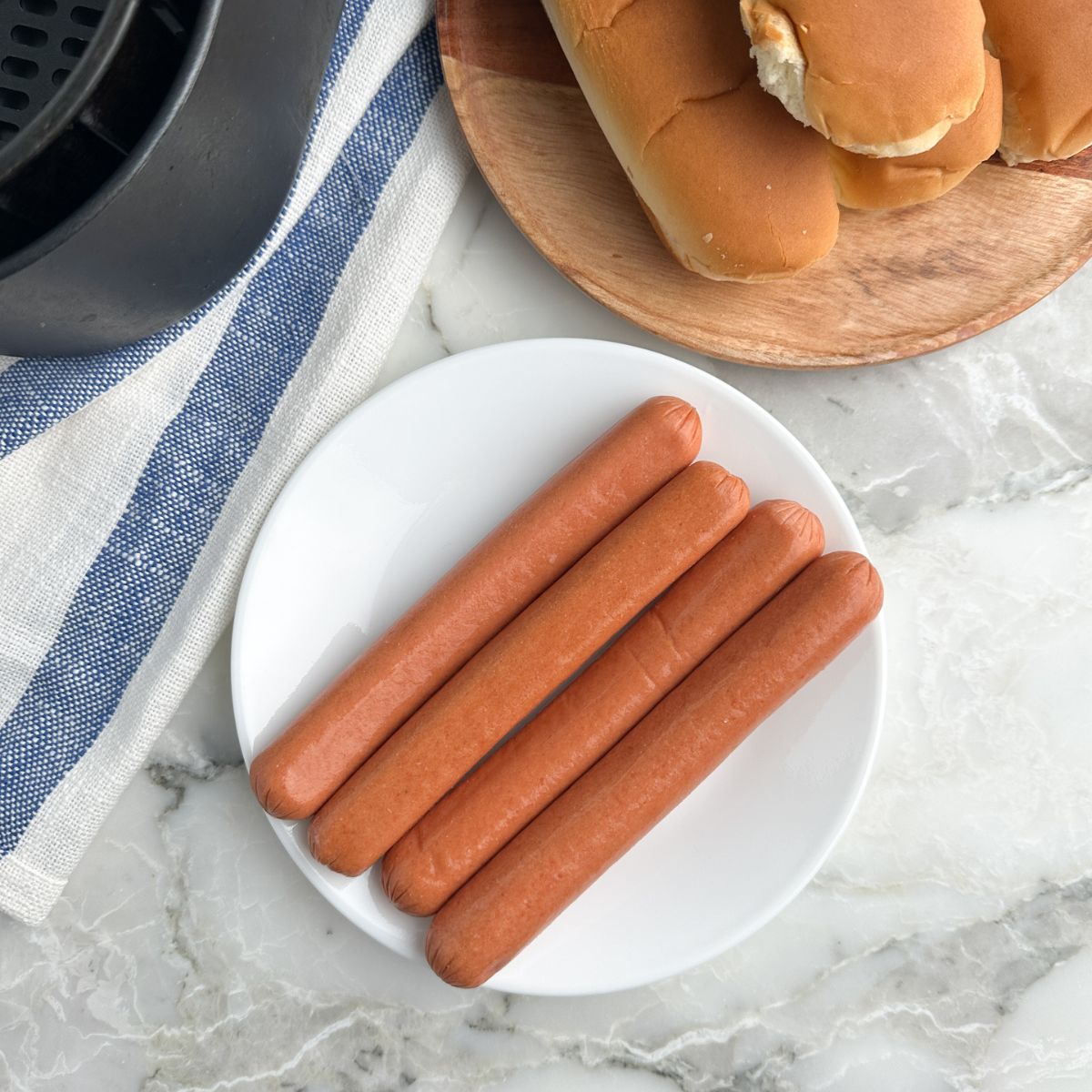 Plate of hot dogs, buns, and air fryer basket.