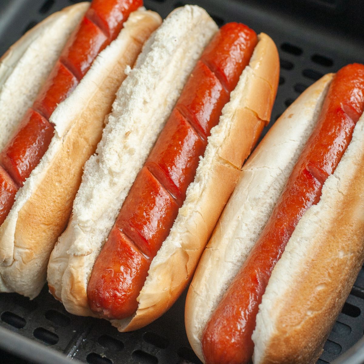 Hot dogs in buns in an air fryer basket.