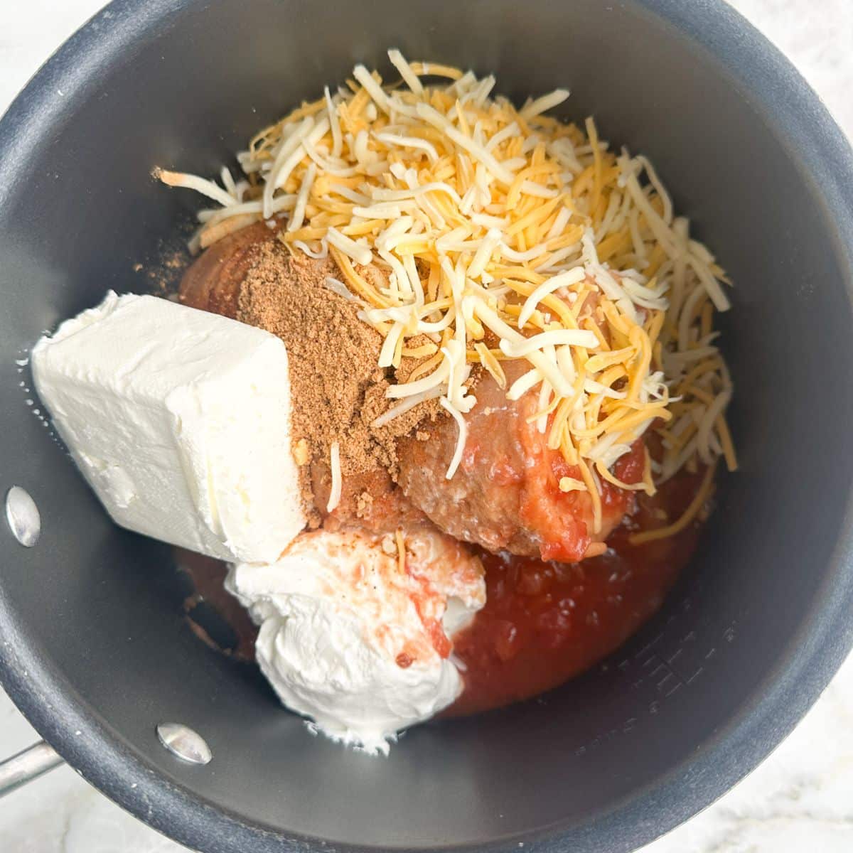 Saucepan with beans, cream cheese, sour cream, and shredded cheese.