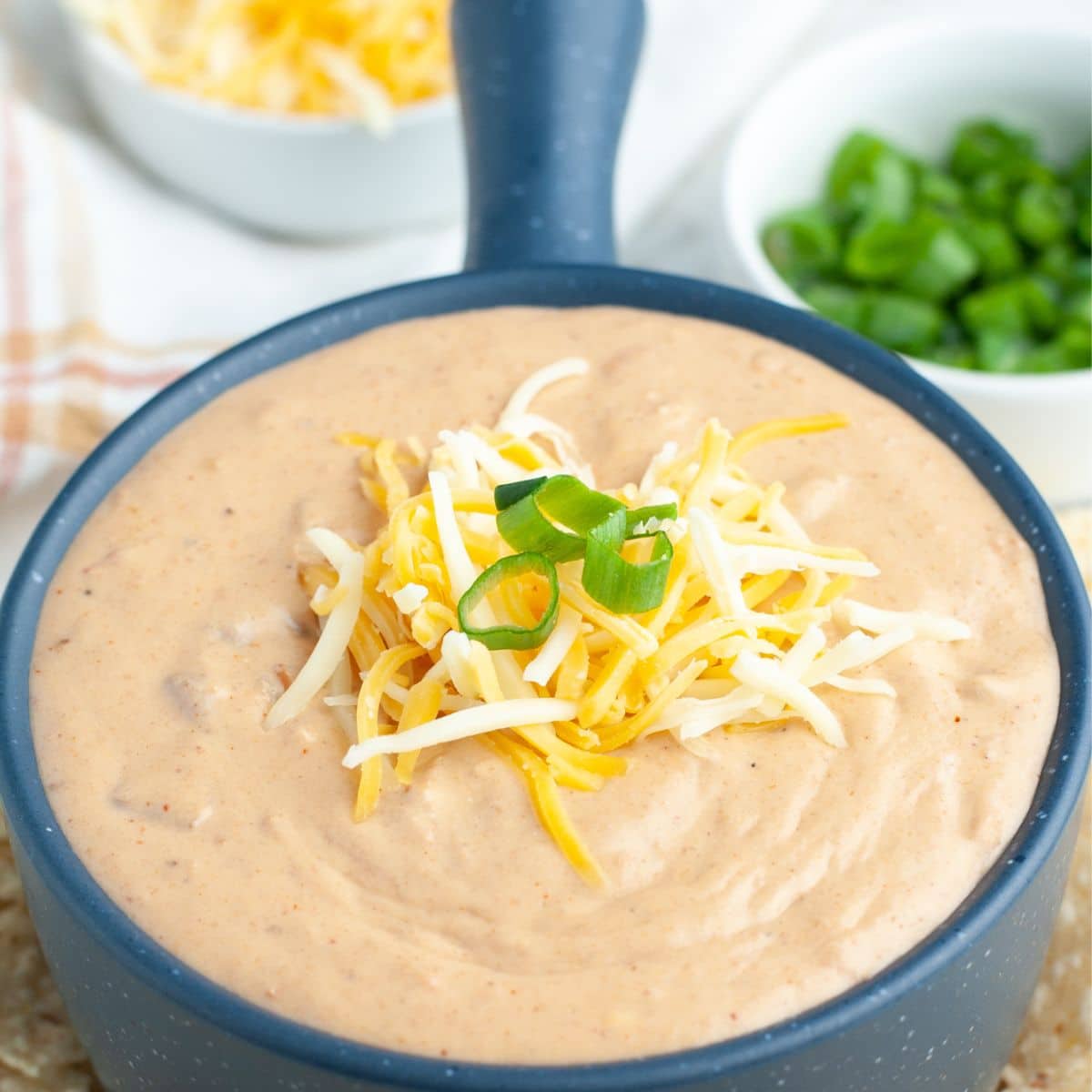 Bowl of refried bean dip topped with shredded cheese and green onion.