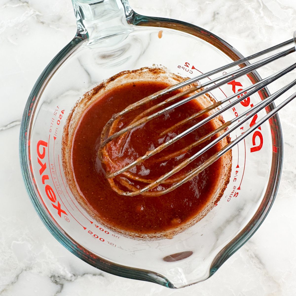 Measuring cup with sloppy joe sauce and a whisk. 