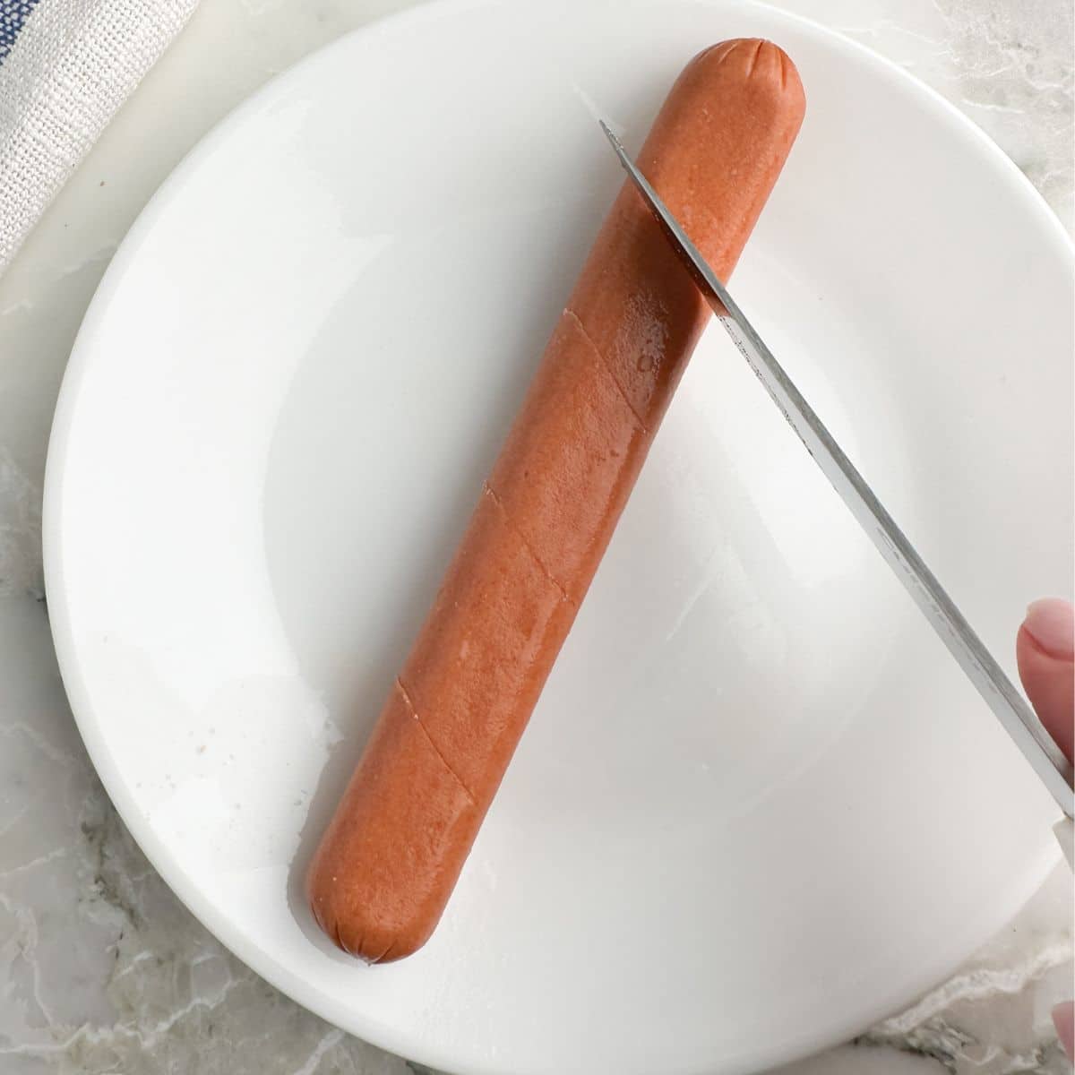 Hot dog on a plate with knife cutting into it. 