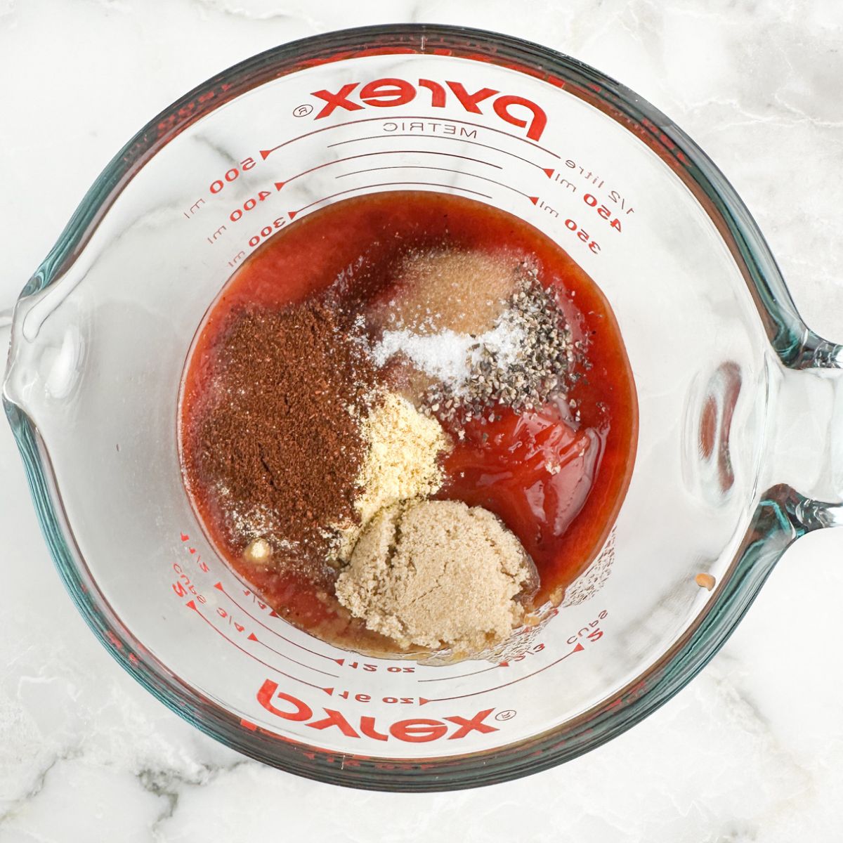 Measuring cup with tomato sauce, brown sugar, and seasonings. 