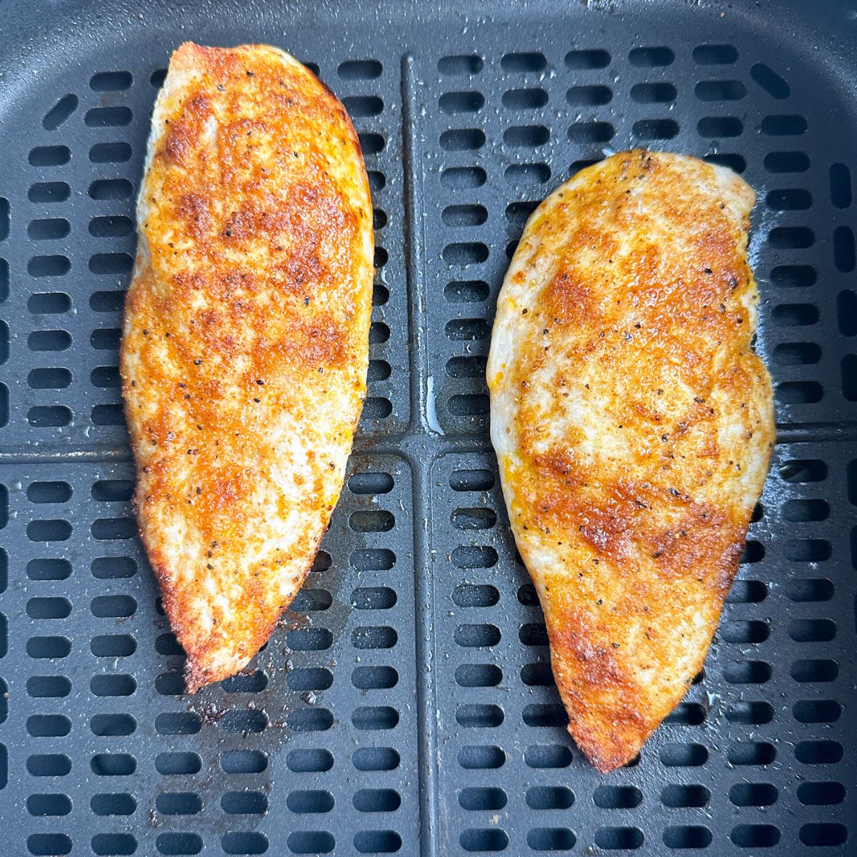 Cooked chicken breasts in air fryer basket.
