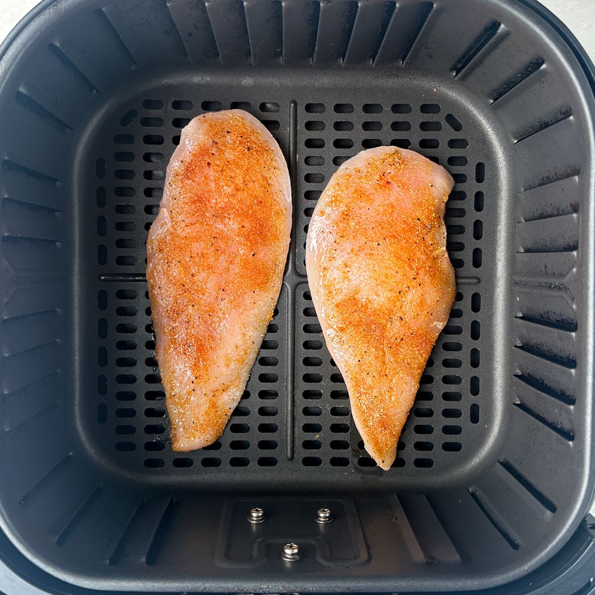 Air fryer basket with seasoning chicken breasts.
