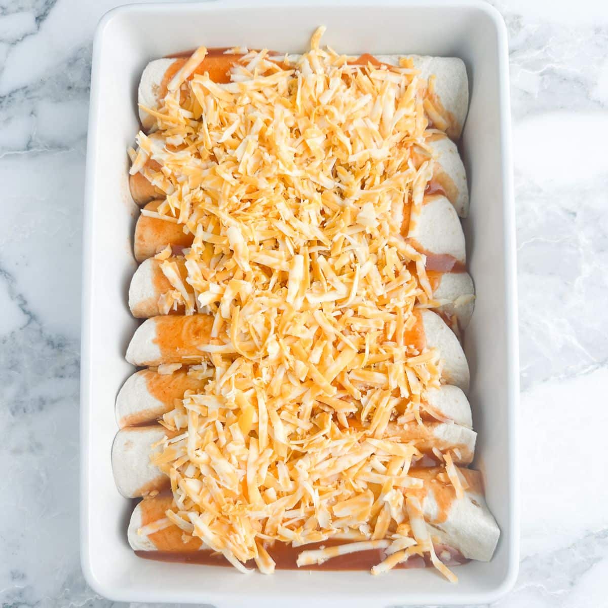 Casserole dish with enchiladas topped with sauce and shredded cheese.