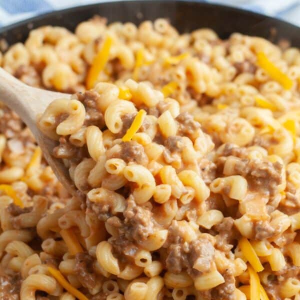 Macaroni noodles with cheese and ground beef. Wooden spoon in a skillet.