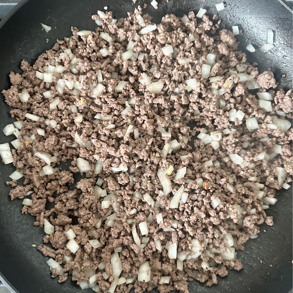 Skillet with ground beef and diced onions. 