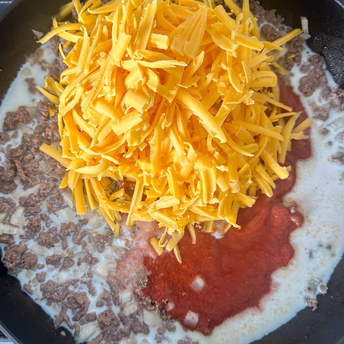 Skillet with ground beef, tomato sauce, and shredded cheese. 