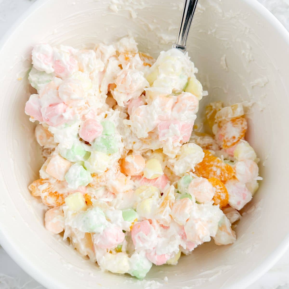 Bowl with a fruit salad made with colorful marshmallows, shredded coconut, and fruit. 