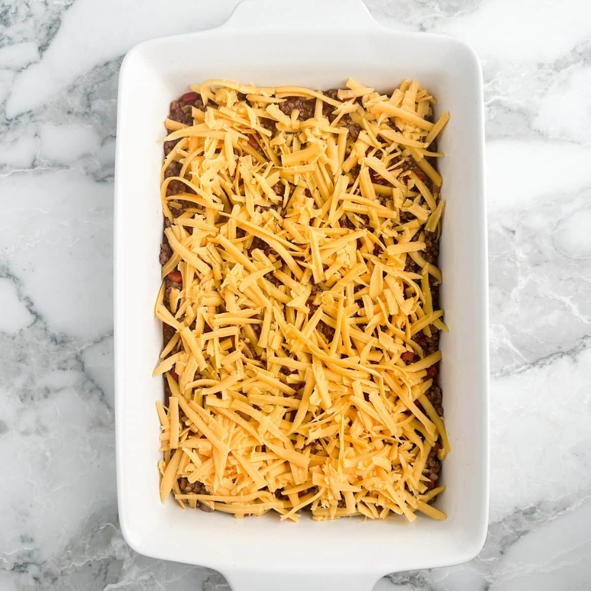 Casserole dish with sloppy joe beef and shredded cheese. 