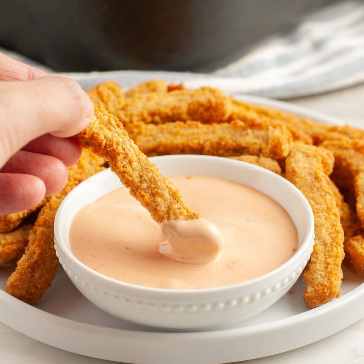 Chicken fry dipping into a bowl of sauce.
