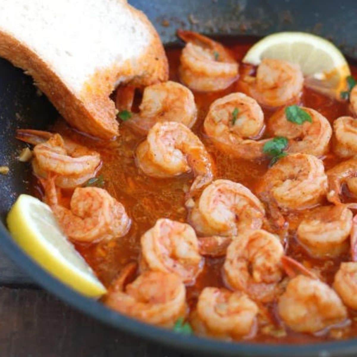 Pan with bbq shrimp, sliced lemon, and piece of bread. 