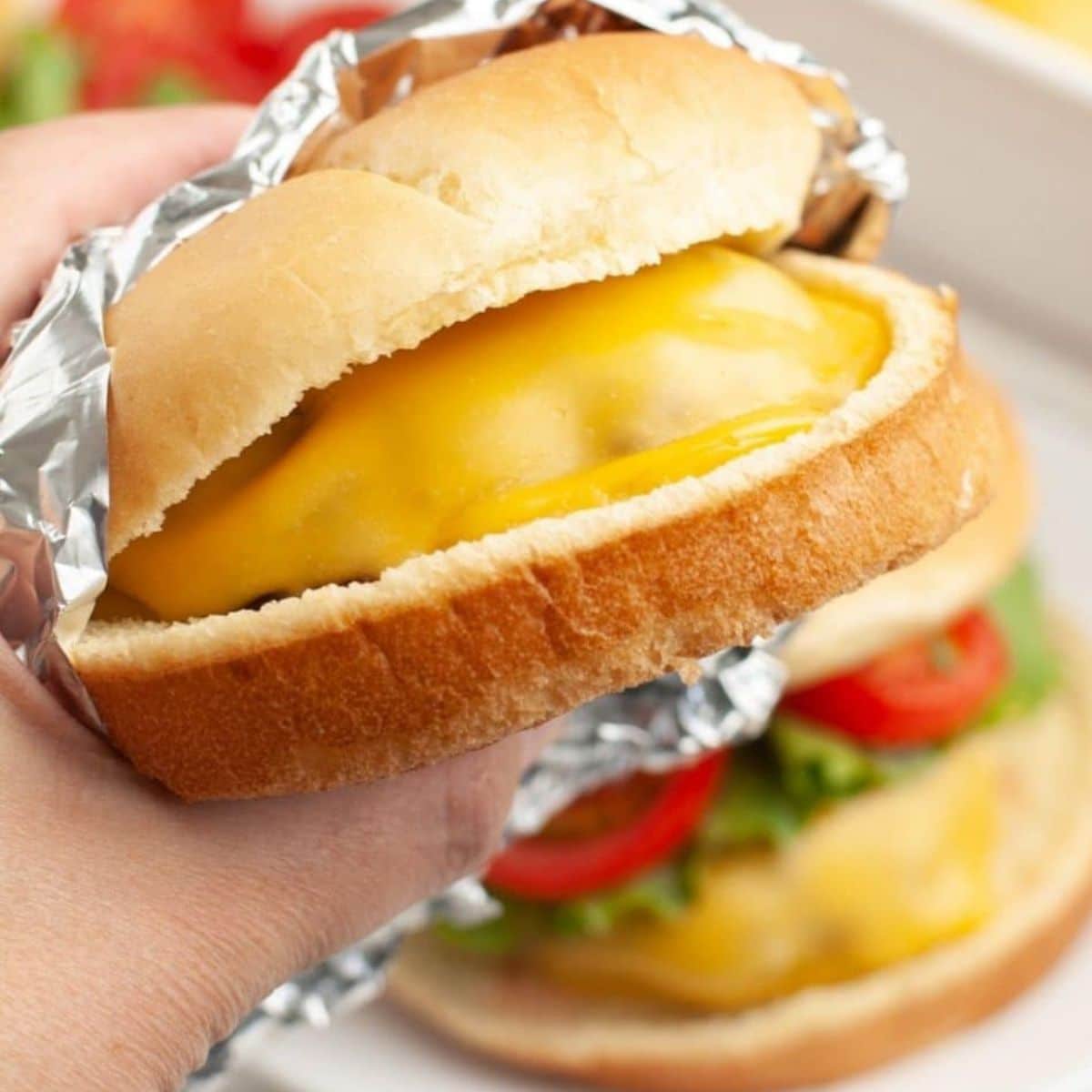 Hand holding cheeseburger wrapped in foil. 