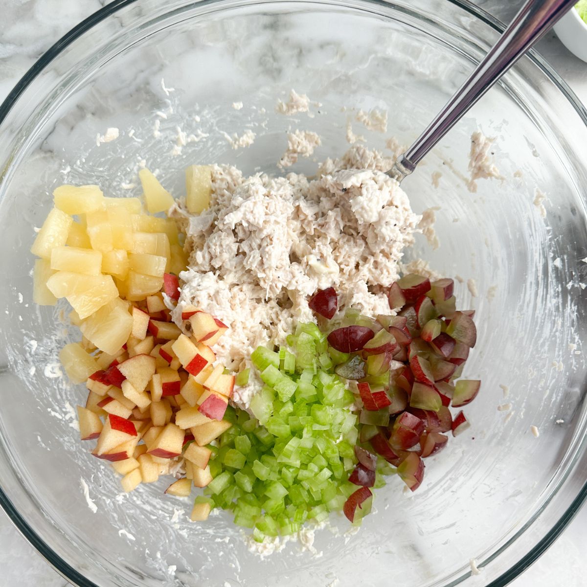 Bowl with diced apples, grapes, celery, pineapple, and chicken.