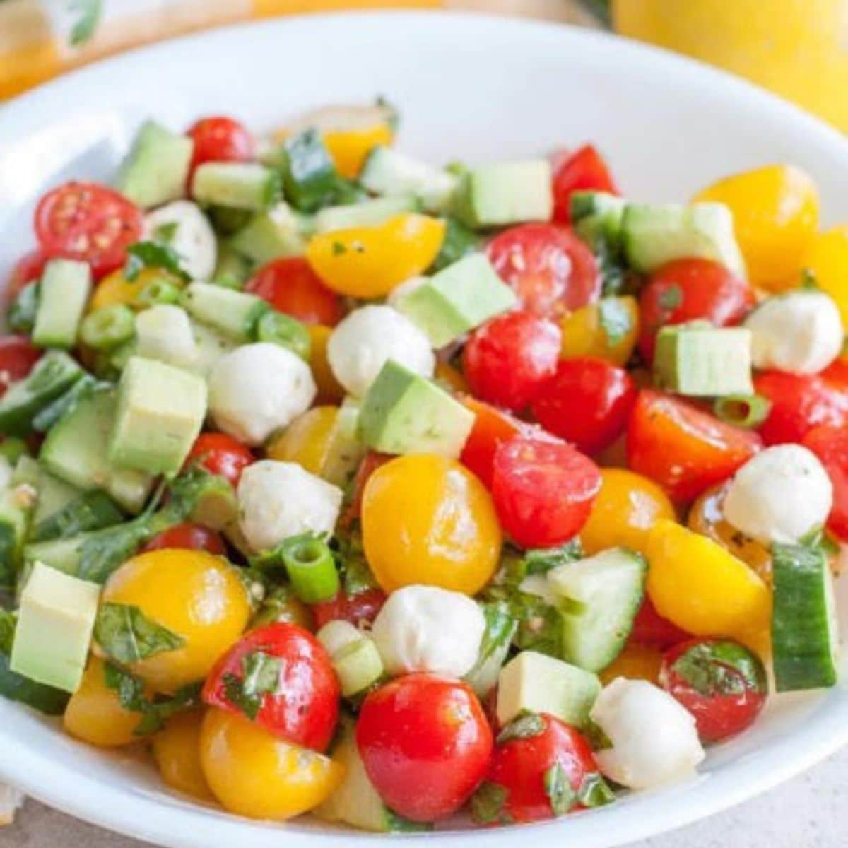 Bowl of cucumber tomato salad with balls of mozzarella cheese.