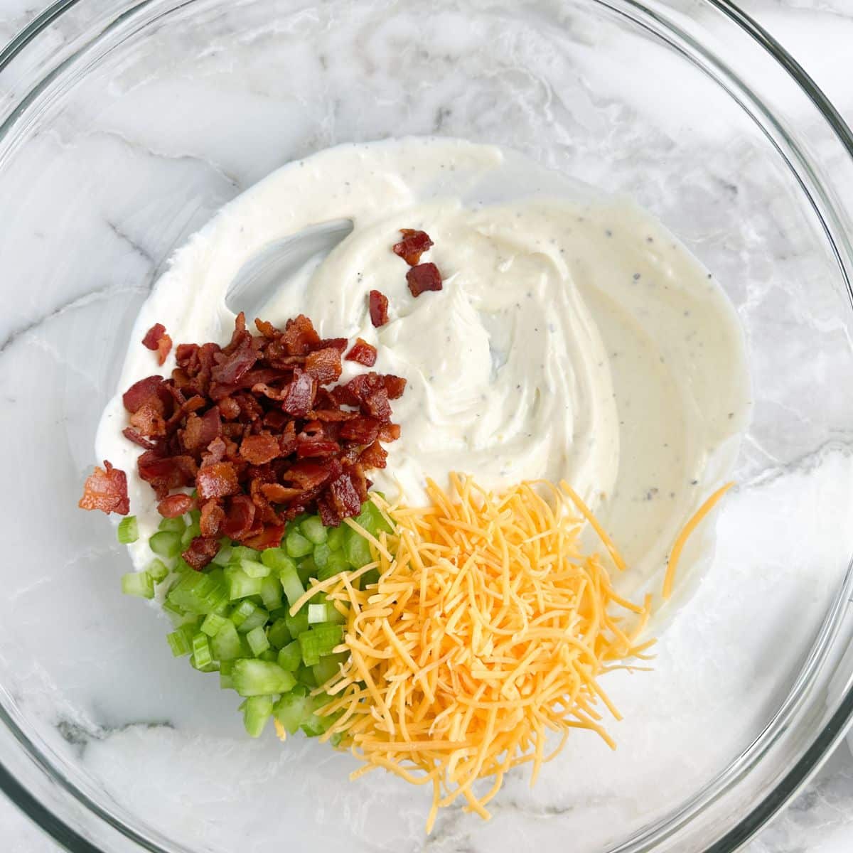 Bowl with mayonnaise, bacon crumbles, celery, and shredded cheese.