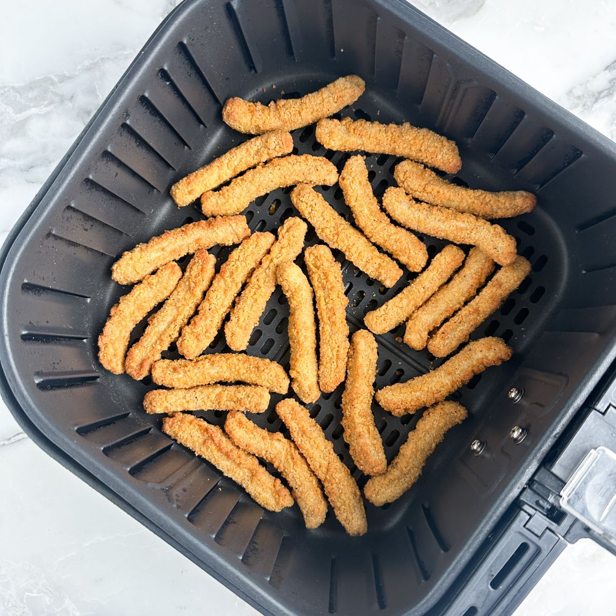 Chicken fries in an air fryer basket.